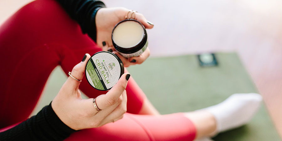 close up view of a person's hands holding a CBD balm and wearing red leggings and white socks